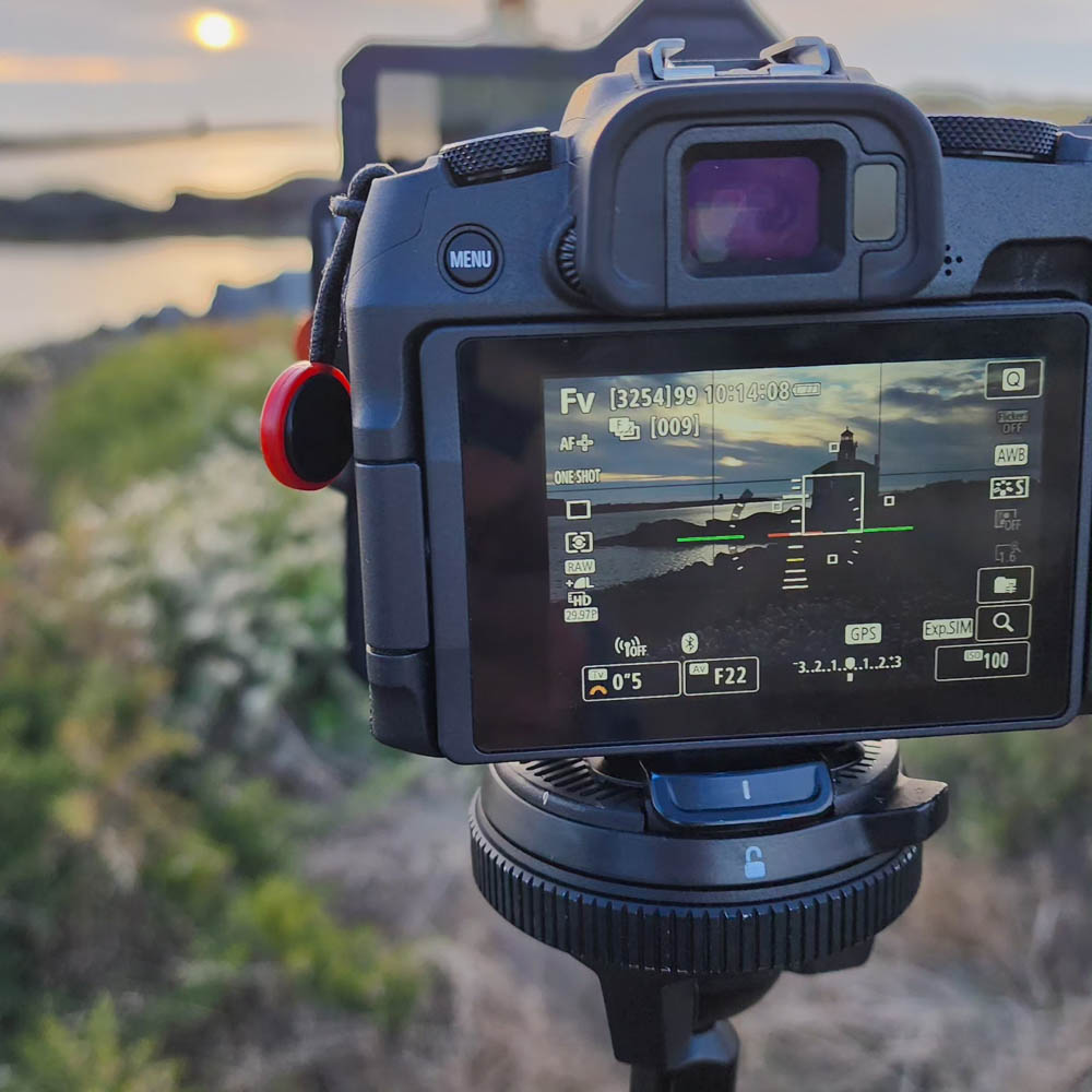 Close-up of camera LCD screen showing a live composition of beach landscape at golden hour.