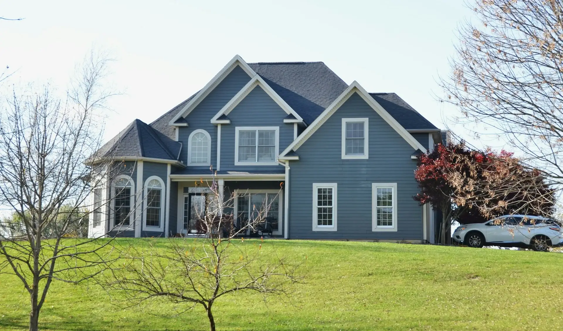 Large blue suburban house with multiple gables and a green front lawn.