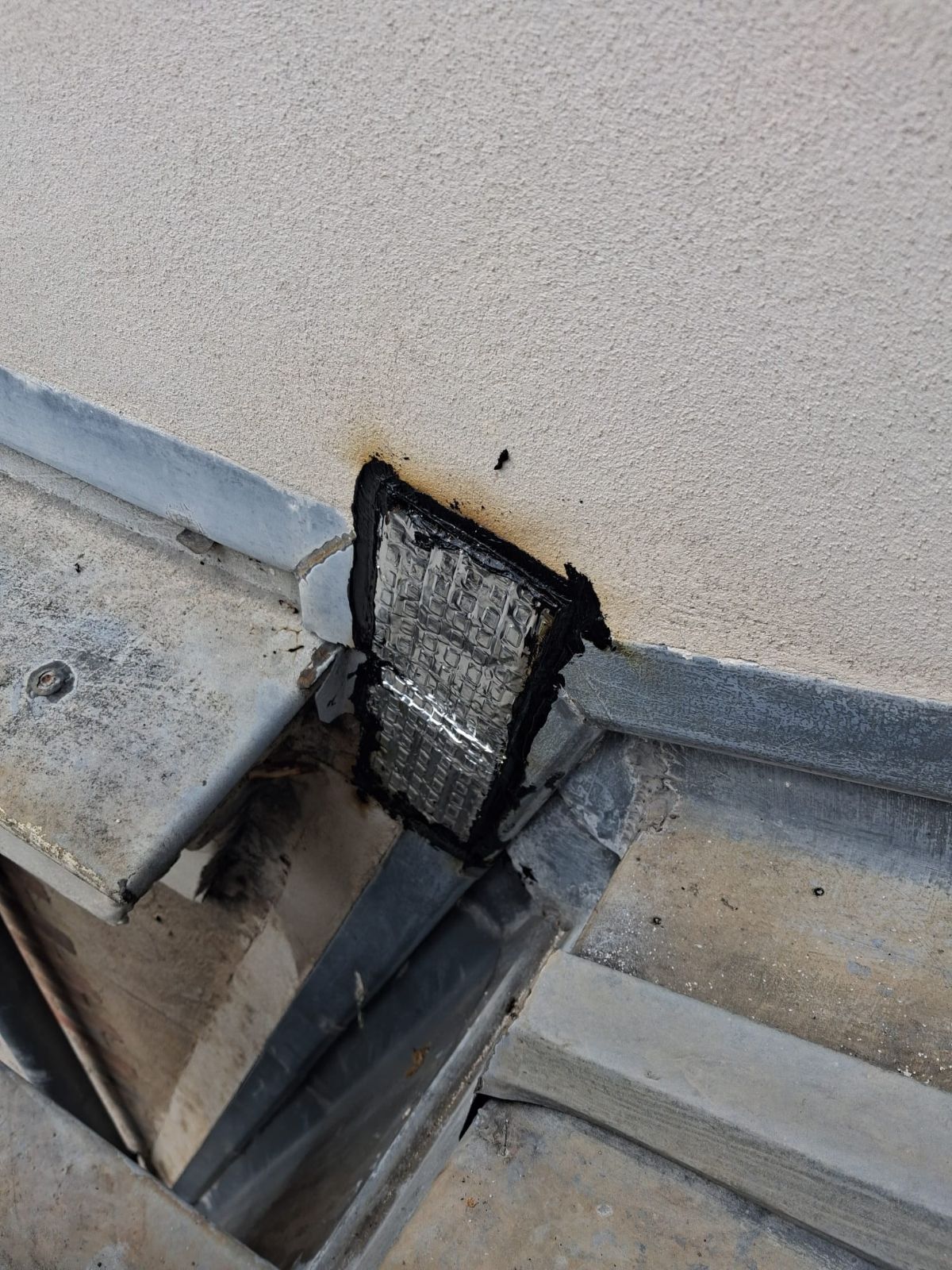 Raccord zinc et maçonnerie repris en mesure conservatoire Réparation d'étanchéité noire renforcée d'une trame au raccord entre une couverture en zinc et un mur enduit