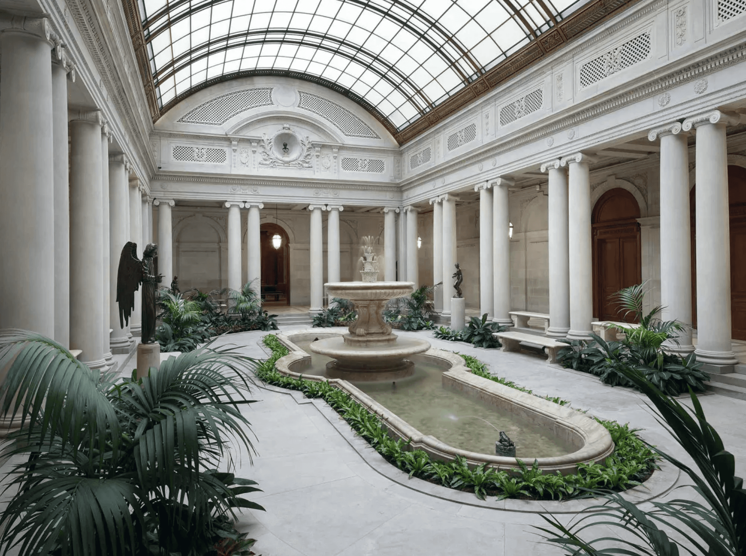 Formal garden at The Frick Collection in New York City, featuring manicured lawn, central fountain, and the museum’s Beaux-Arts mansion framed by trees and iron gates.