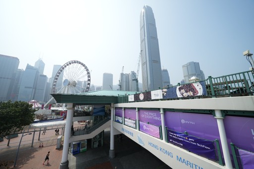 View of the Hong Kong waterfront showing the Hong Kong Maritime Museum entrance decorated with purple Pyth Network banners reading “The Price of Everything” and “Innovative Finance Day.” The skyline, Ferris wheel, and IFC Tower rise in the background under hazy daylight.