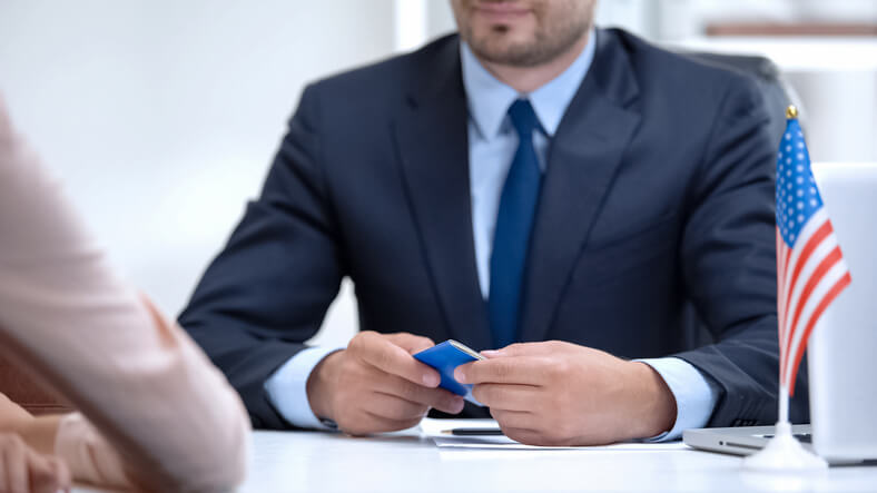 A man in a suit holds a passport, looking confidently at the camera. Form G-28