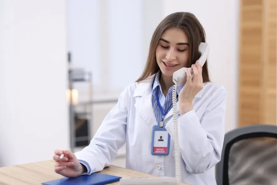 AI admin assistant for healthcare shown as a medical assistant in a white lab coat speaking into a desk phone.