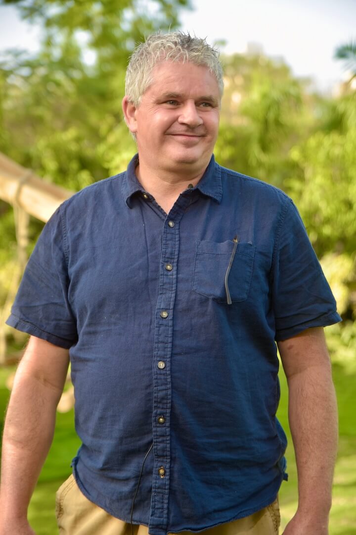 Man in blue collared shirt and tan shorts smiling outdoors