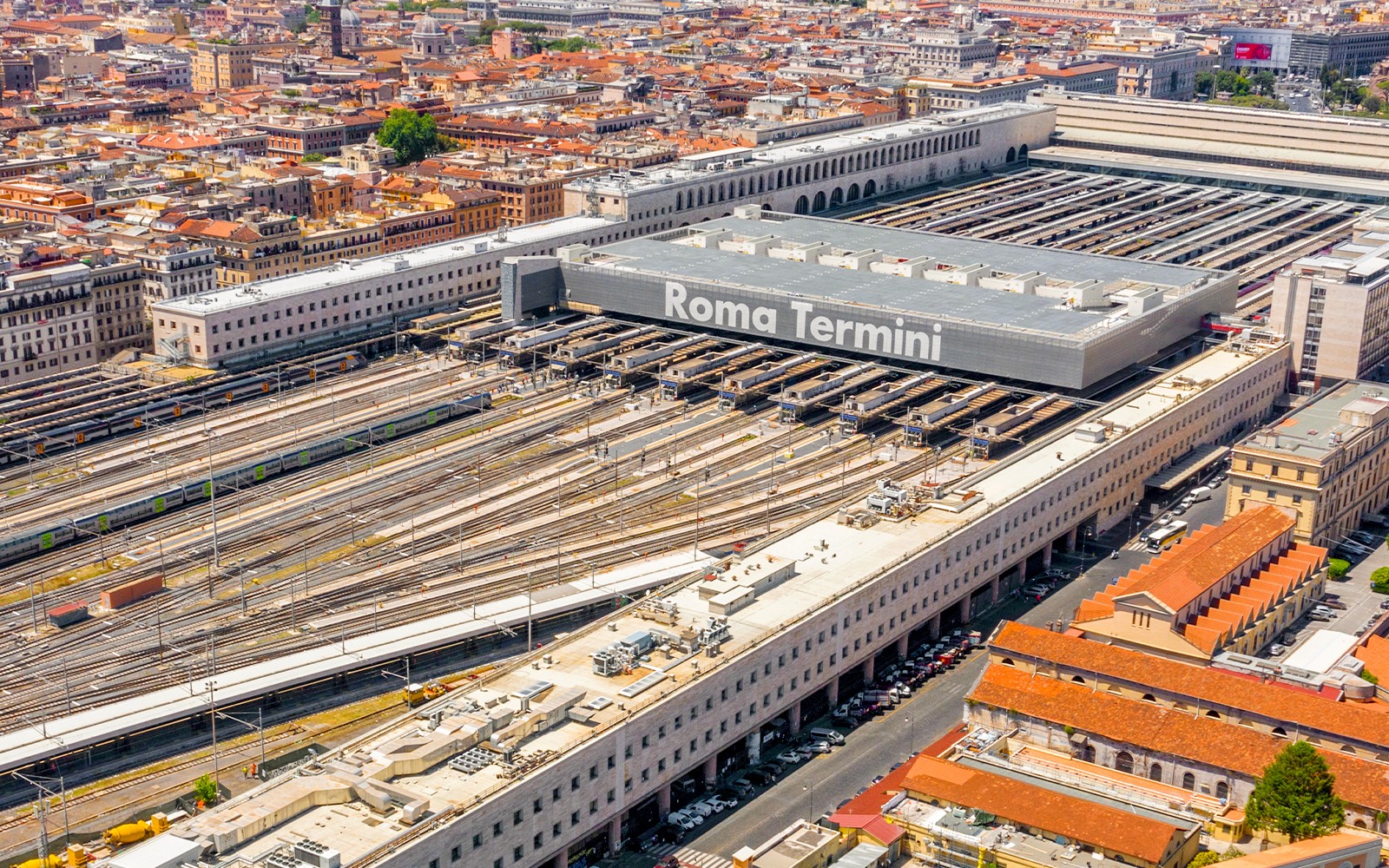 ภาพถ่ายมุมสูงของสถานีรถไฟโรม่า เทอร์มินี (Roma Termini) พร้อมเส้นทางรถไฟหลายสายและทัศนียภาพของเมืองที่รายล้อม