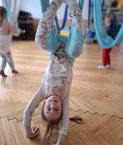 Dítě visící hlavou dolů v modré síti při lekci fly jógy