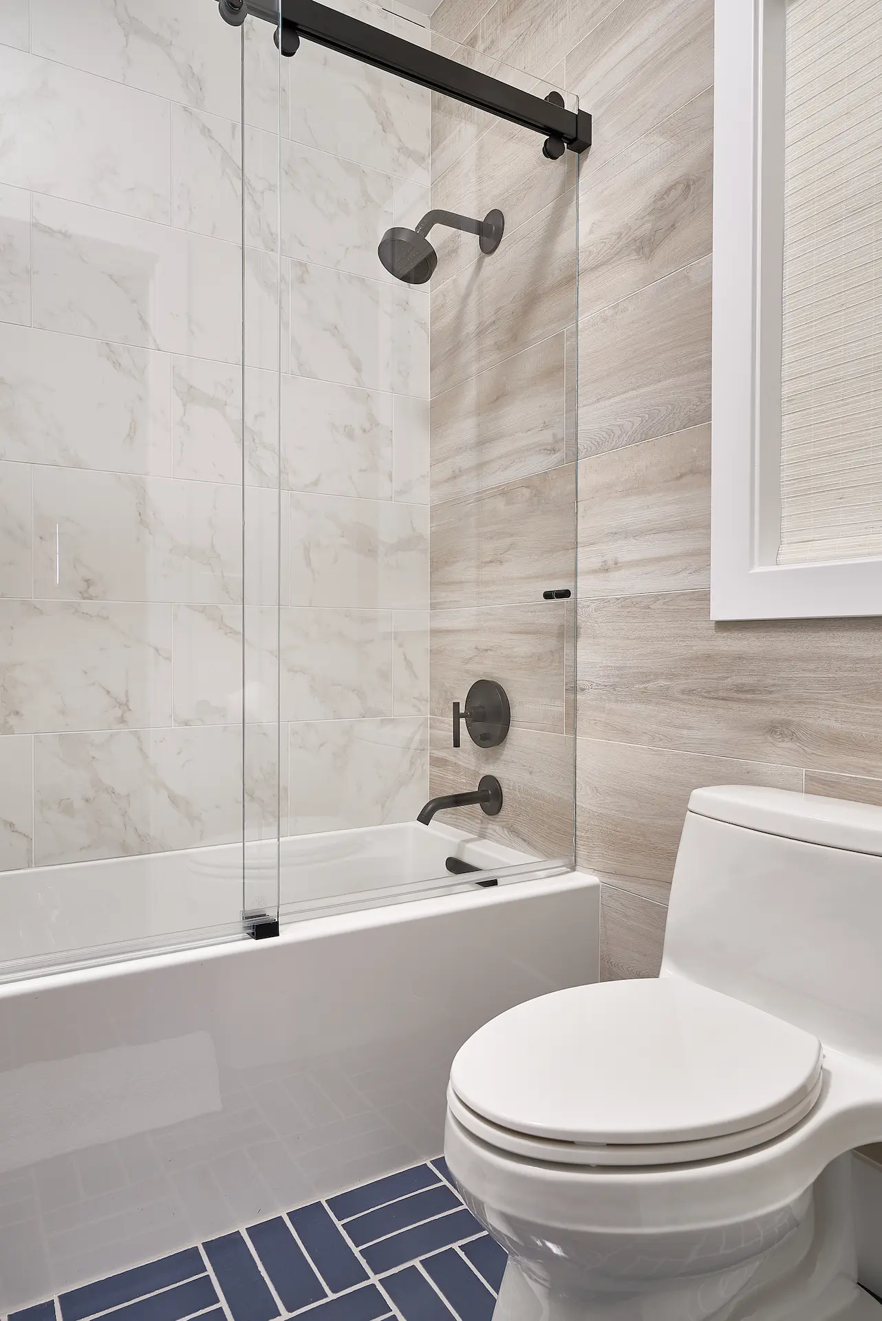View of the shower area in the kids' bathroom, showcasing the shower head and tile design in the Irvine Contemporary Coastal Remodel. Photo by Todd Huge.