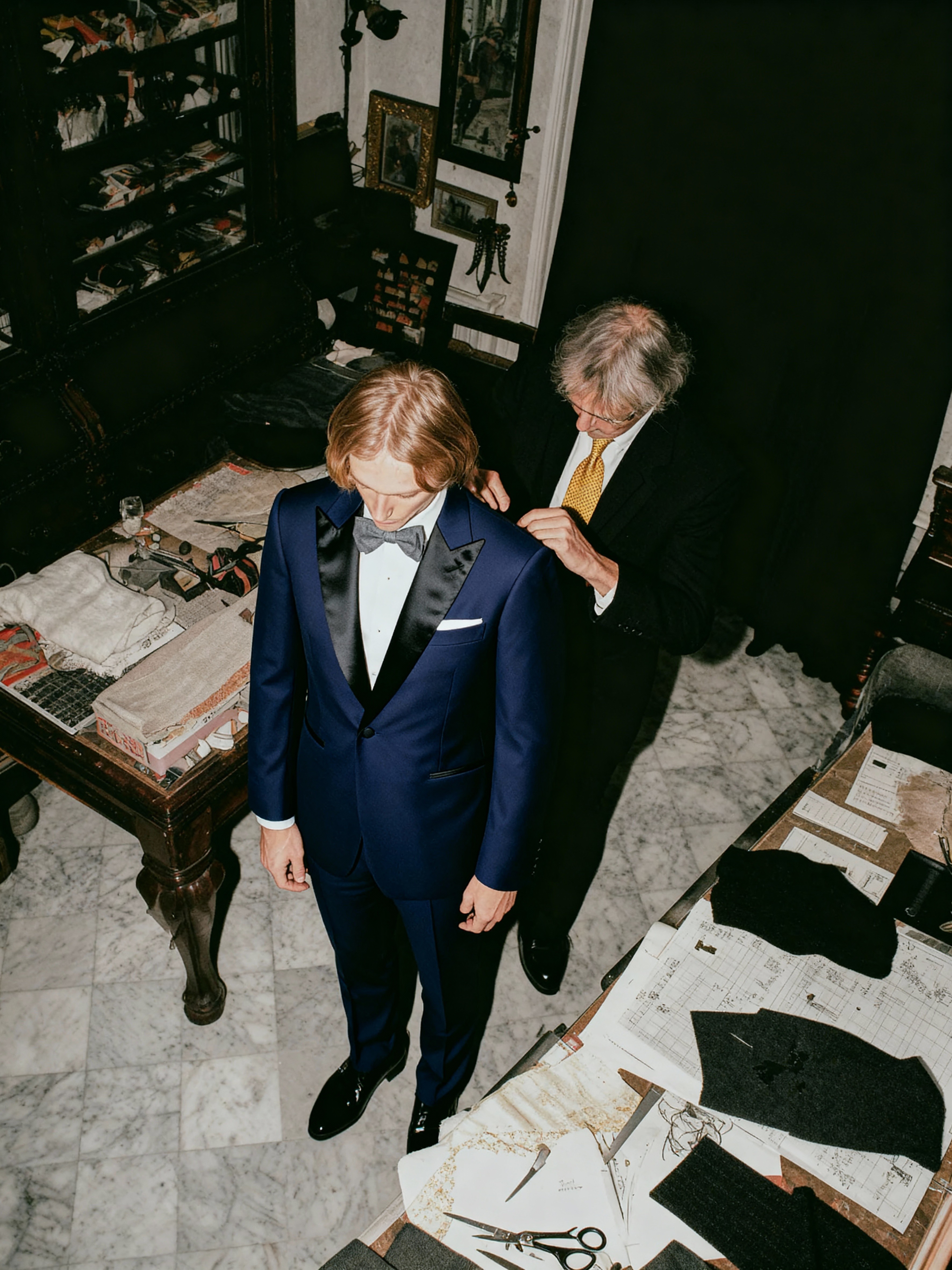 AI-generated fashion image showing a tailor fitting a man in a navy tuxedo inside an Italian atelier, created by Myrovia Labs for a luxury menswear campaign. AI fashion creative direction, digital production, luxury tailoring visuals.