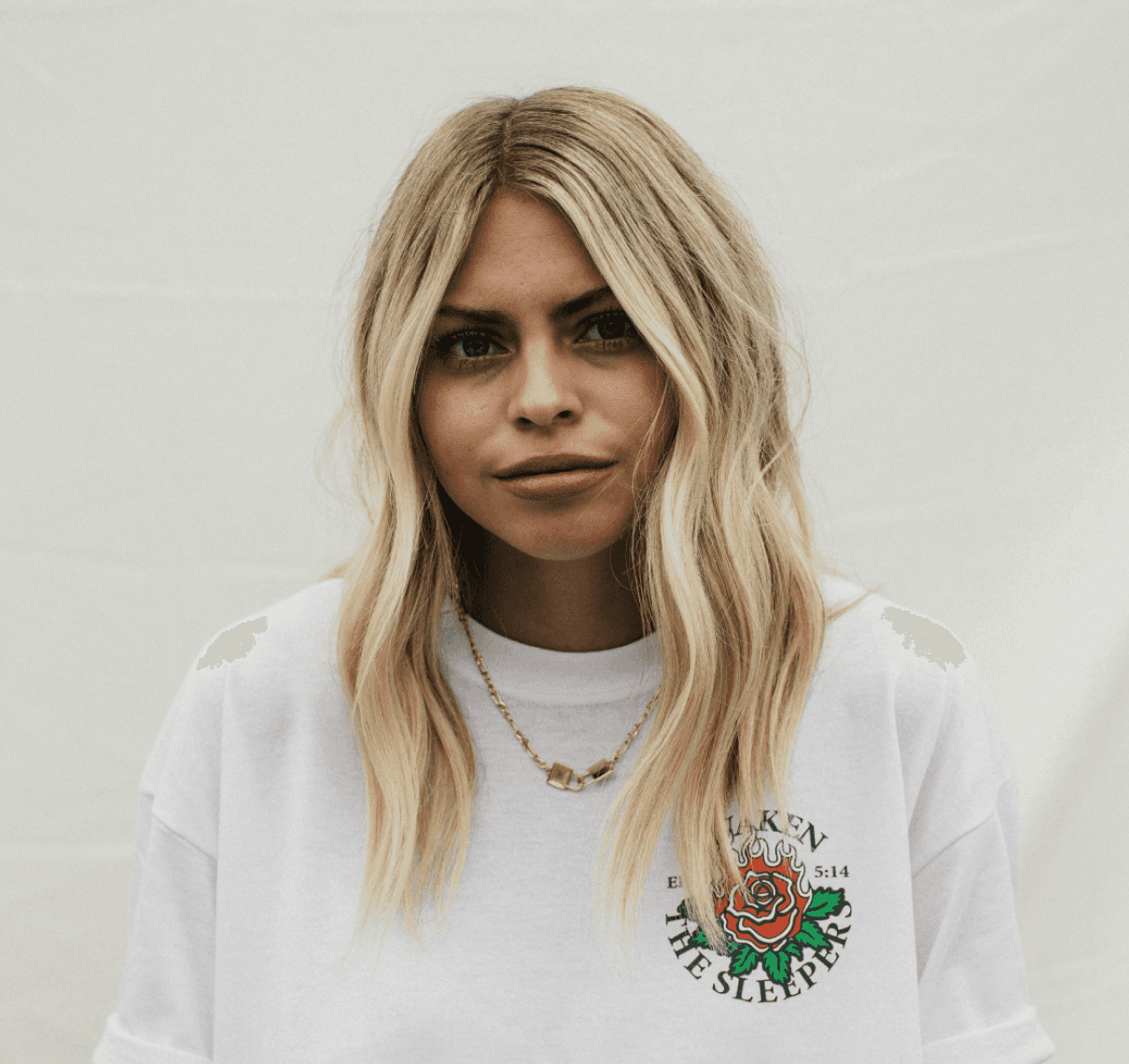 Woman with bleached blond hair and visible brown roots, wearing a white T-shirt, facing forward