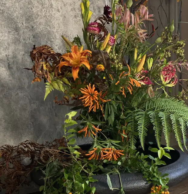 Arreglo floral con flores naranjas y rosadas en maceta negra para ambientación natural de interior con estilo contemporáneo.