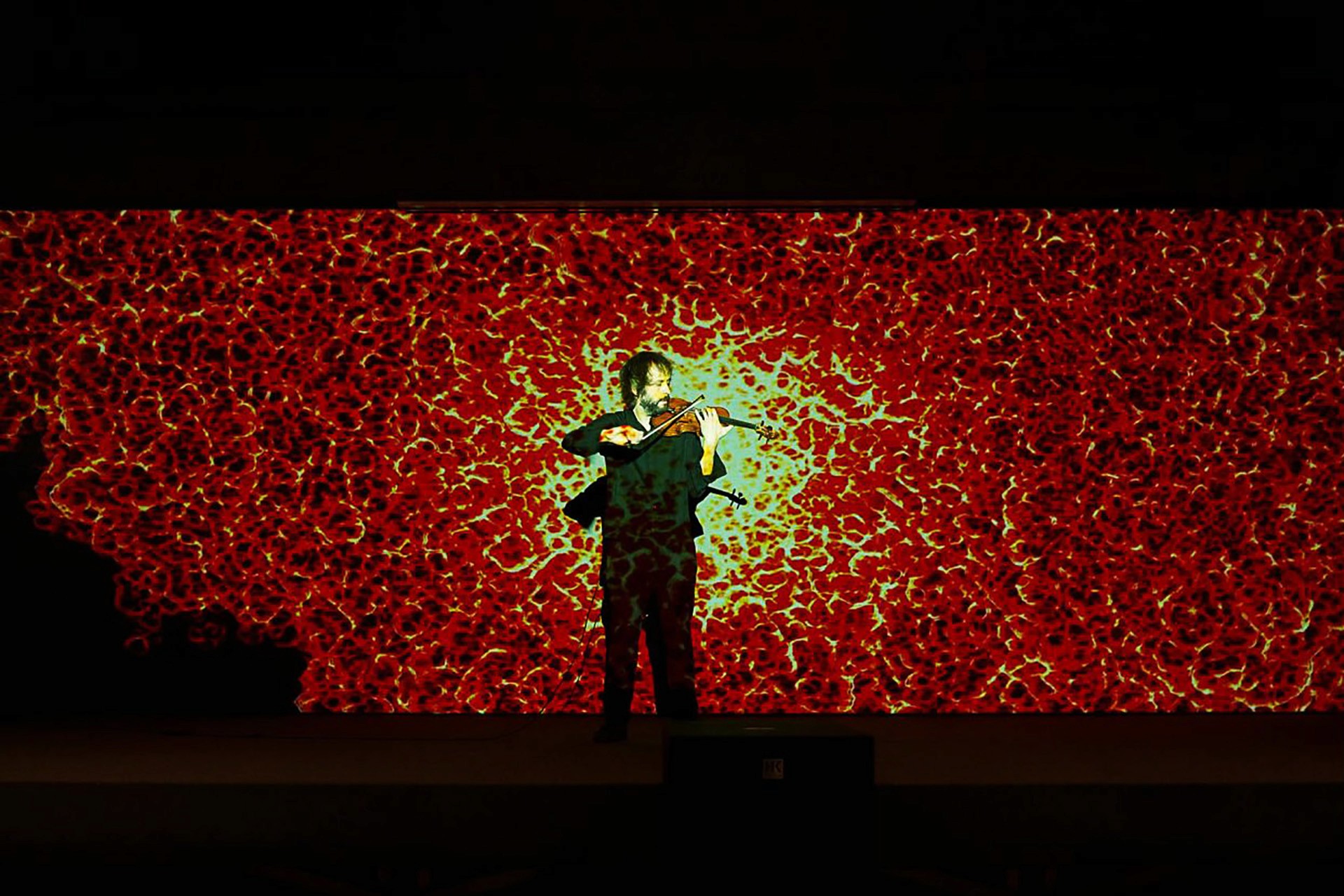 Man playing the violin in front of the projection of a large digital fireball