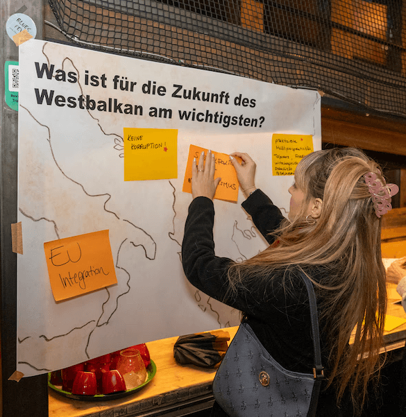 Junge Frau klebt Post-it auf ein Plakat mit der Aufschrift "Was ist für die Zukunft des Westbalkan am wichtigsten?"