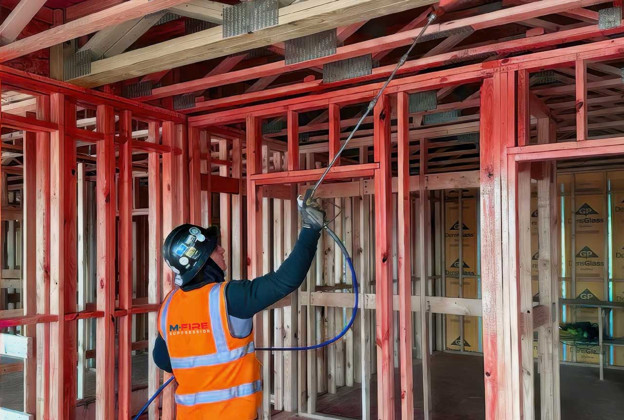 A professional worker in safety gear applying fire retardant spray to a wood-frame interior construction site