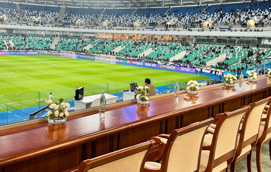 VIP stadium view withcushseats, floraldecor, and a soccermatch in progress