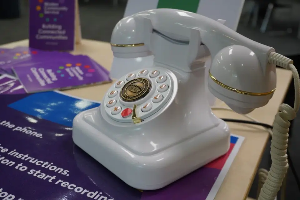 An old school phone sitting on a poster asking for people to record an answer to a question.