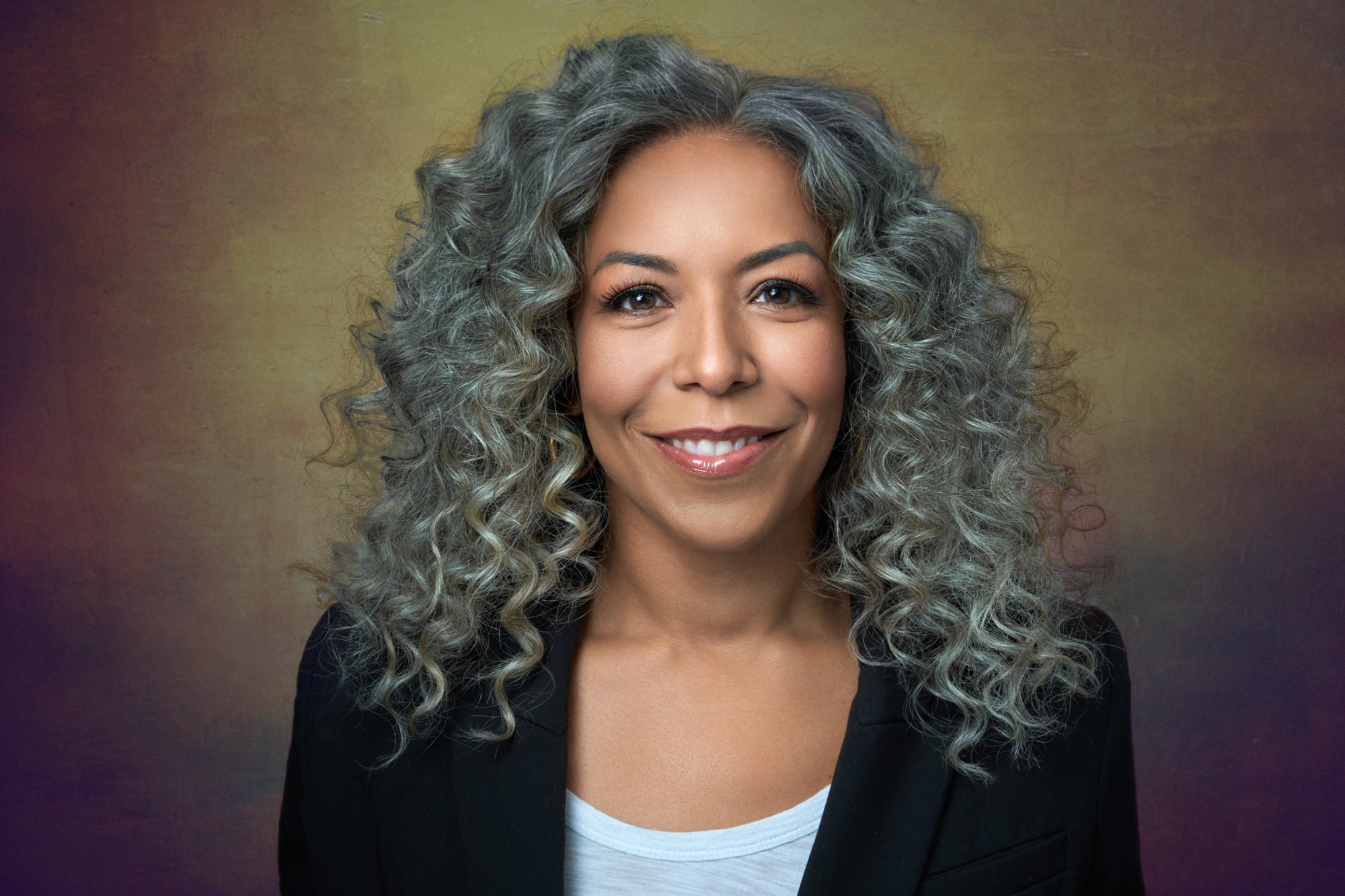 Powerful executive portrait of a female leader with grey curls and a floral scarf, signaling experience and defiant authority. CEO headshot photographer.