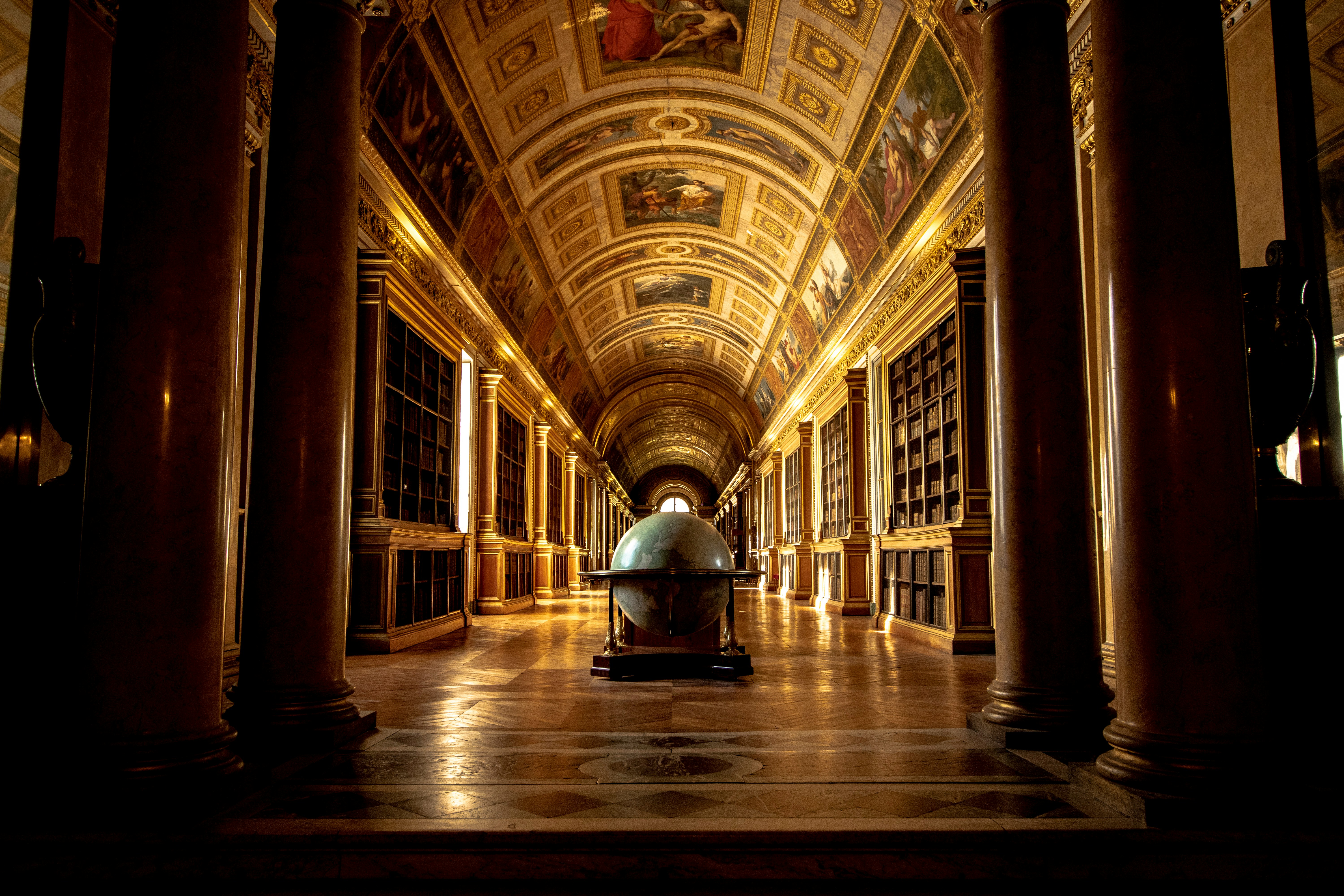 An ornate golden hallway with a globe in the foreground inside the Fontainebleau Castle in France.
