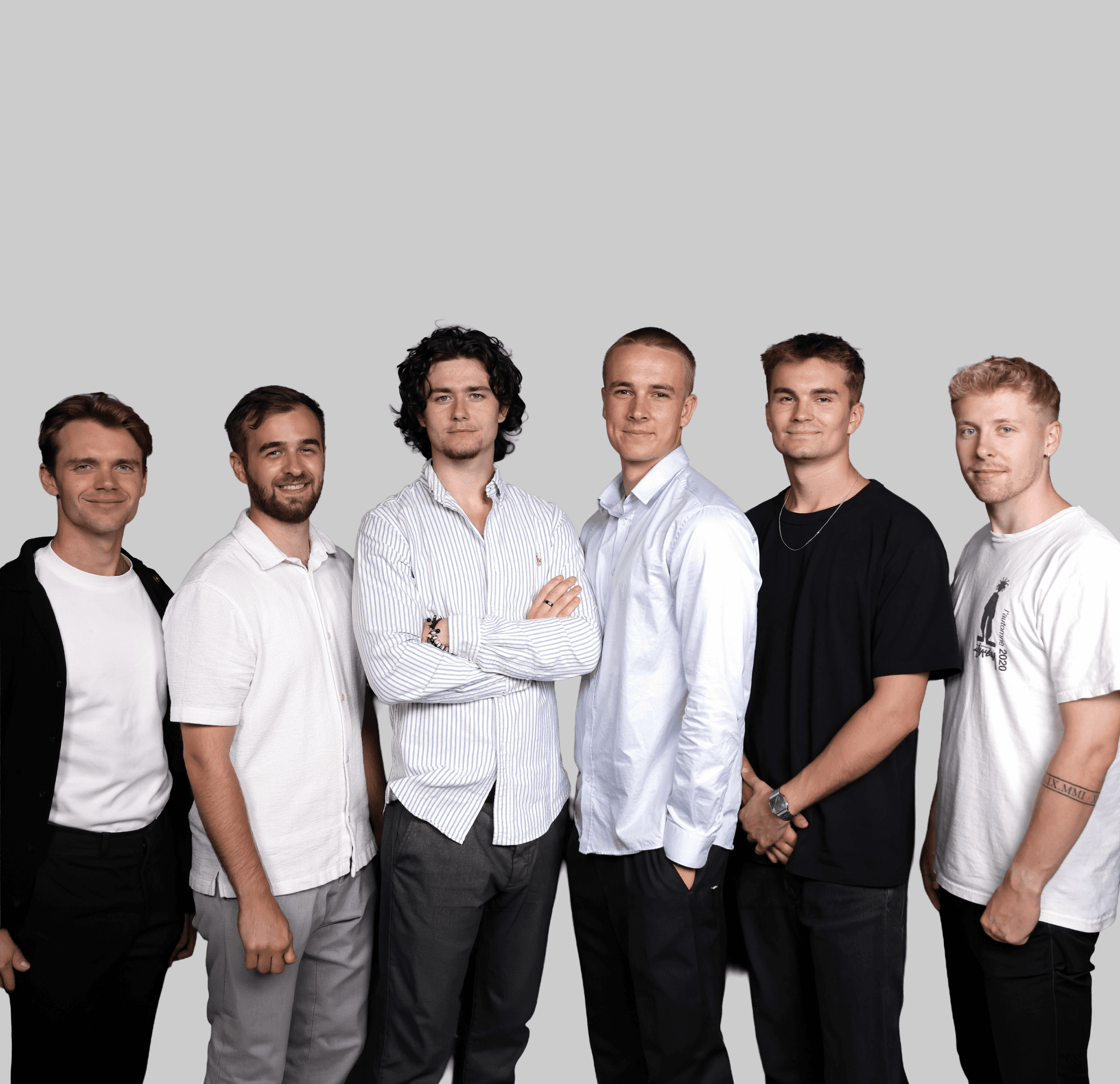 A group of six men standing in a row, dressed in various casual outfits, against a plain gray background.