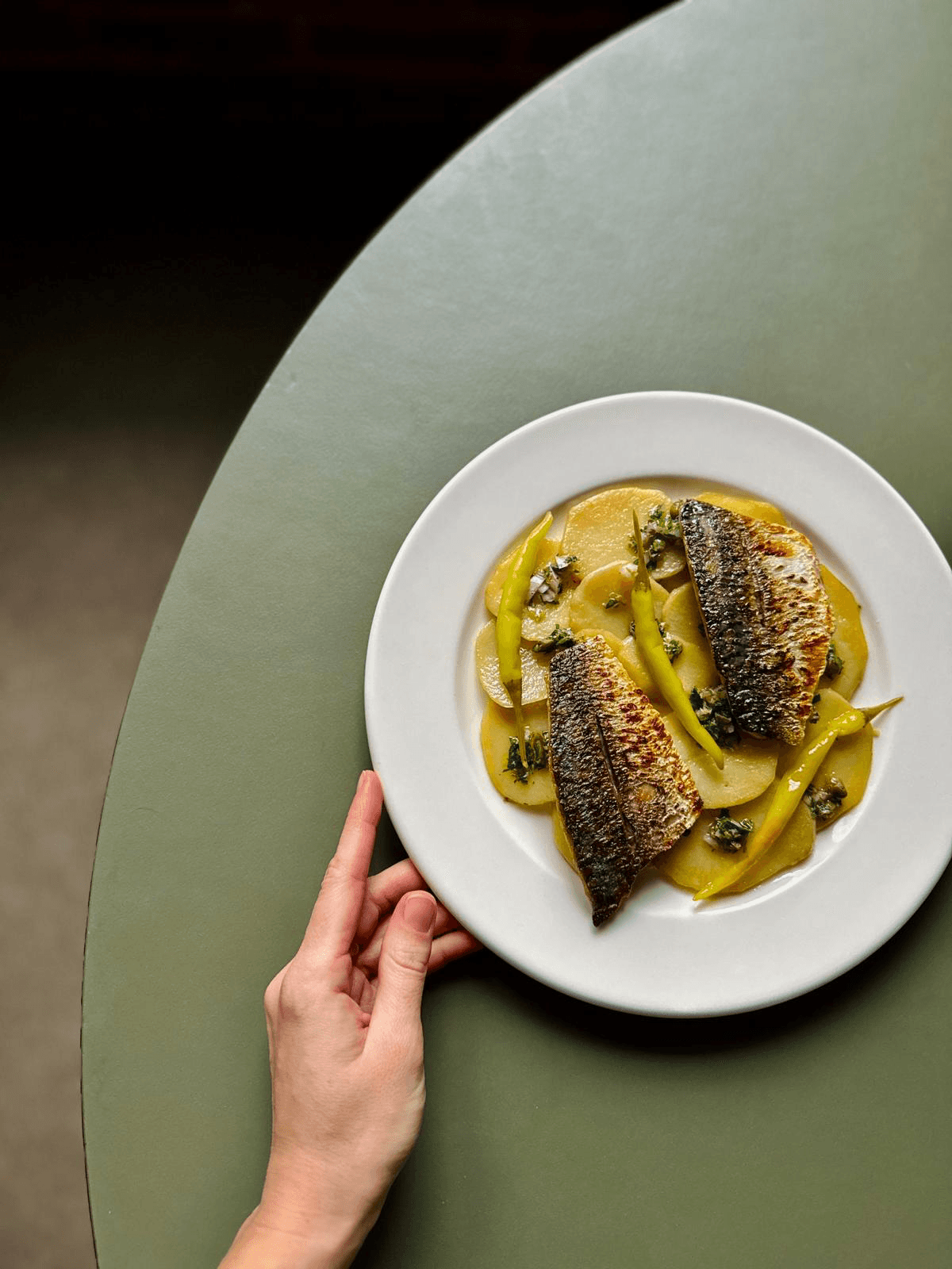 Two people sit at a table conversing, sharing a meal in a cozy setting with brick walls and plates of food.