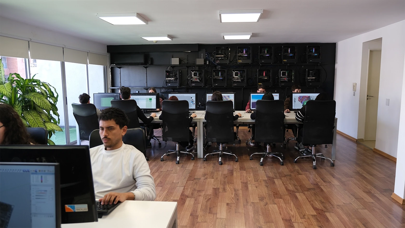 3D artists working at high-performance workstations inside the 3D CBA studio, with wall-mounted render servers in the background.