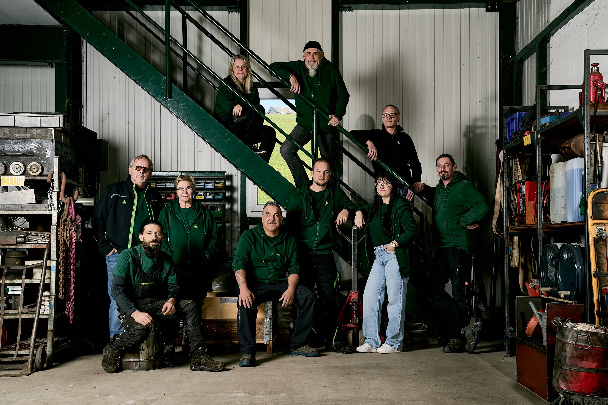 Gruppe von Personen in grünen Oberteilen posiert für ein Foto, einige sitzen oder stehen auf einer Treppe und auf dem Boden.