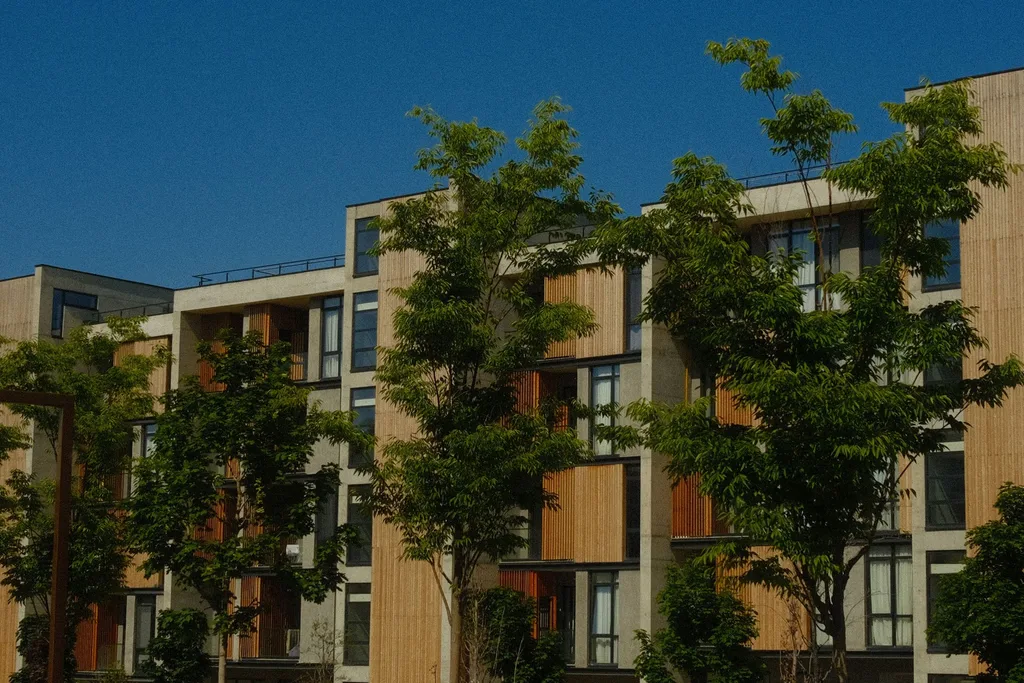 Red brick facade partially hidden behind trees under a clear blue sky.