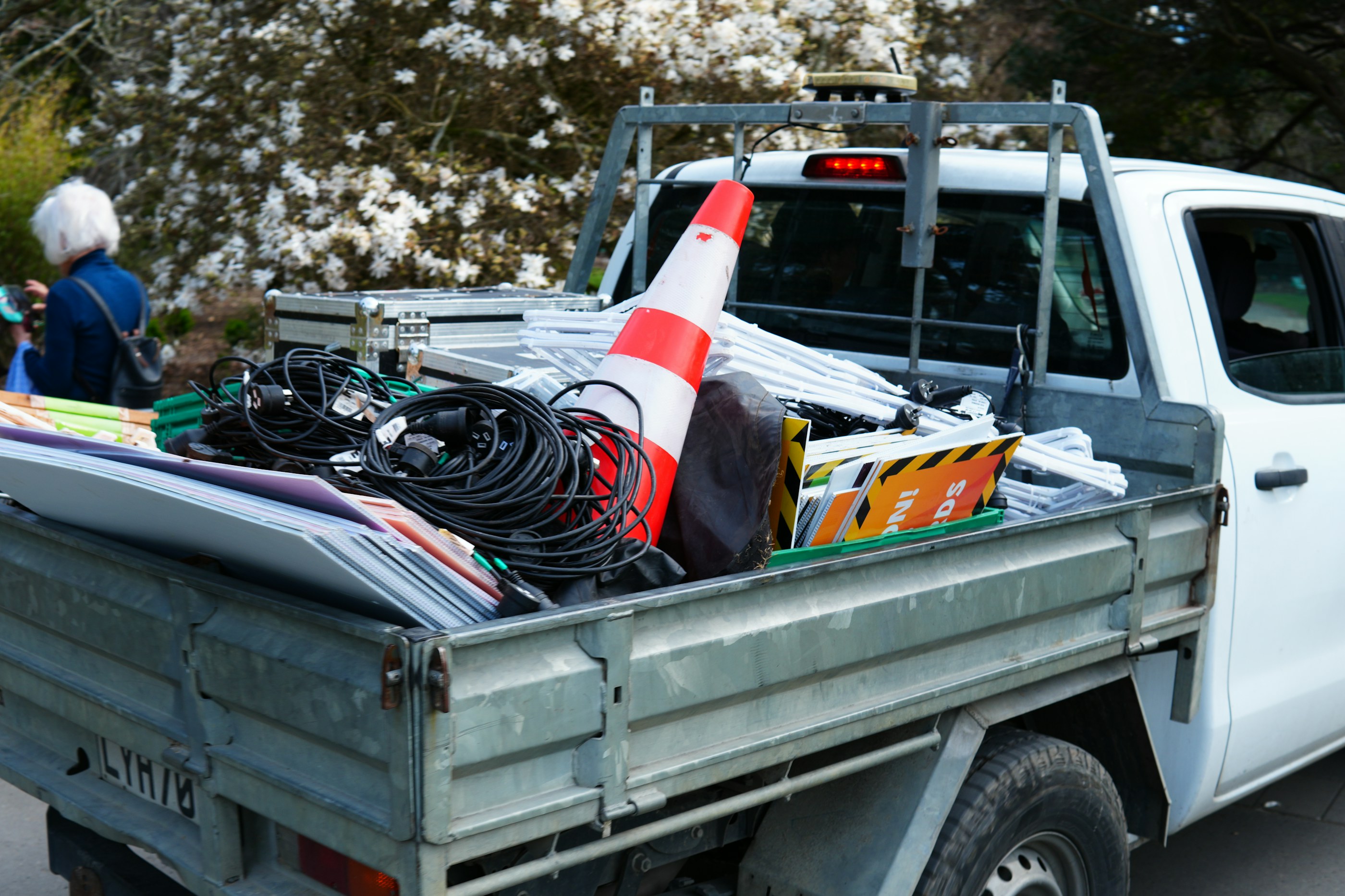 A contractor's pickup bed loaded with cable reels, sign boards and a traffic cone