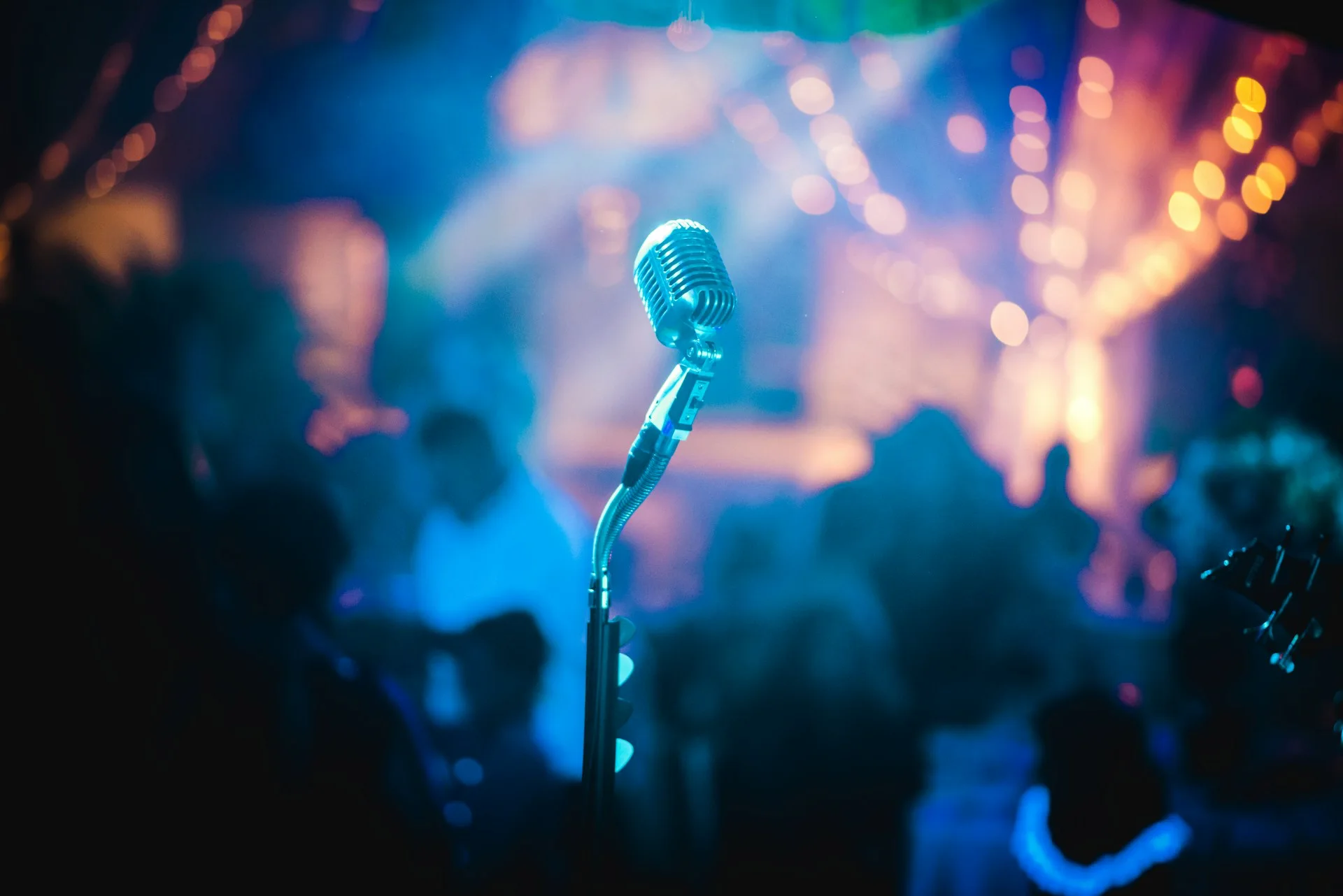 Microphone on stage with blurred crowd and colorful lights in a bar during a live music event.