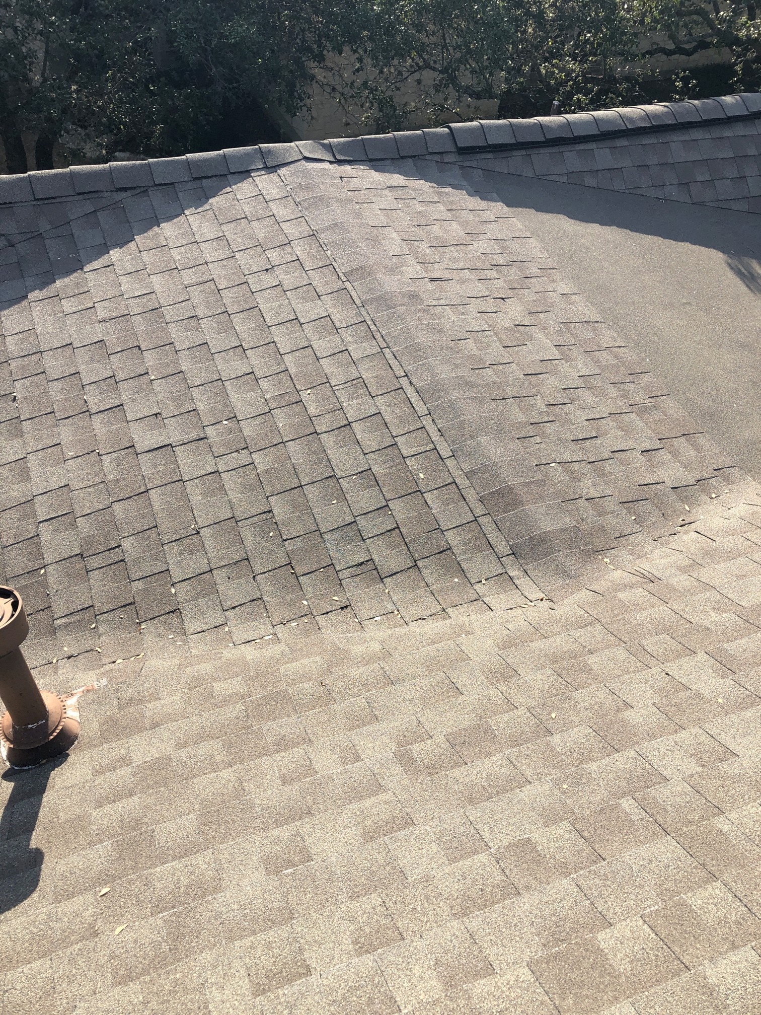 Warm gray architectural shingles shown across a hip and adjoining slopes in sun and shade; manufacturer not verified.