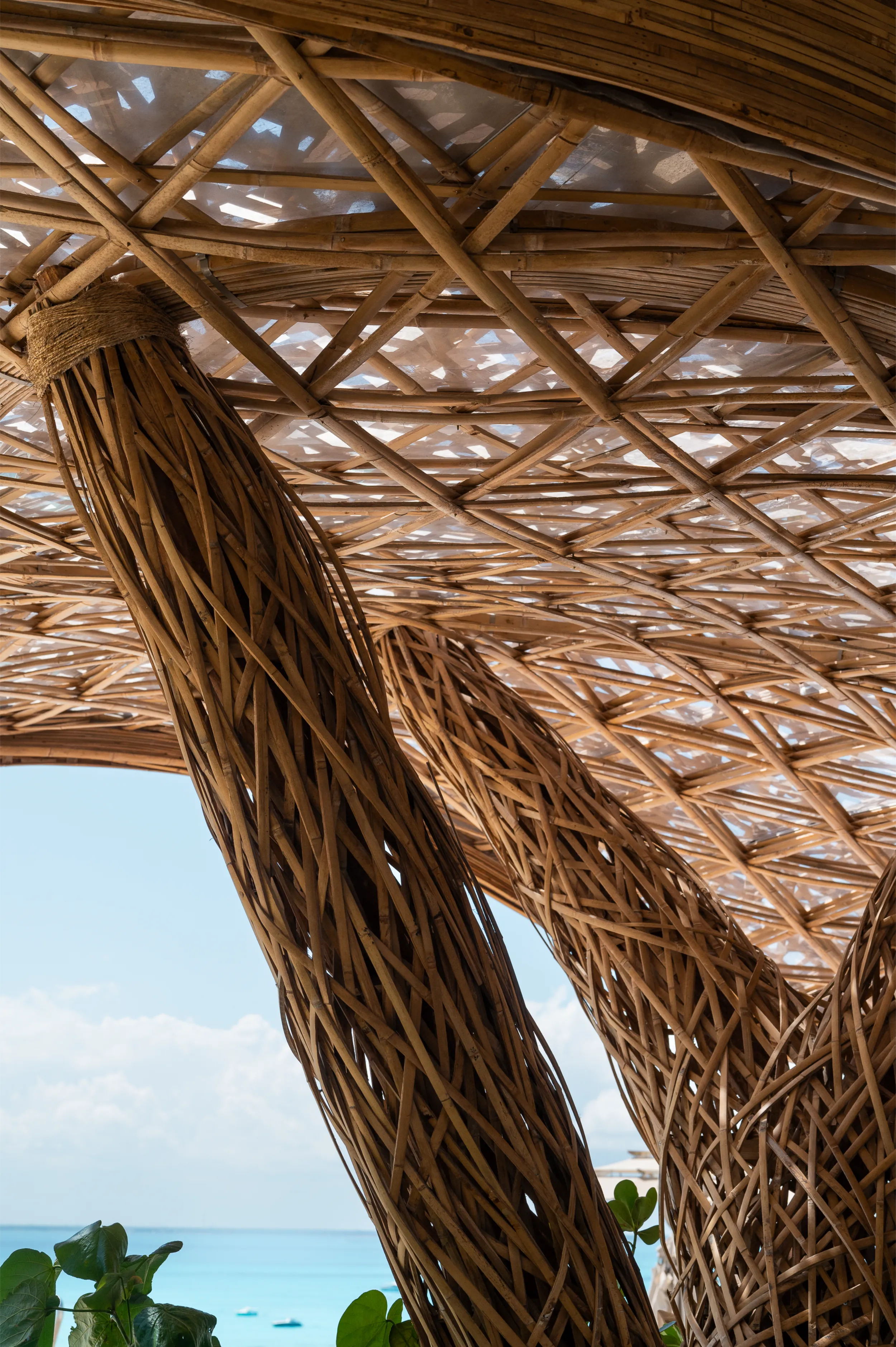 Close-up architectural detail of a branching bamboo pillar by Arquitectura Mixta, highlighting the intricate texture and structural precision of the handcrafted material palette against a clear blue sky.