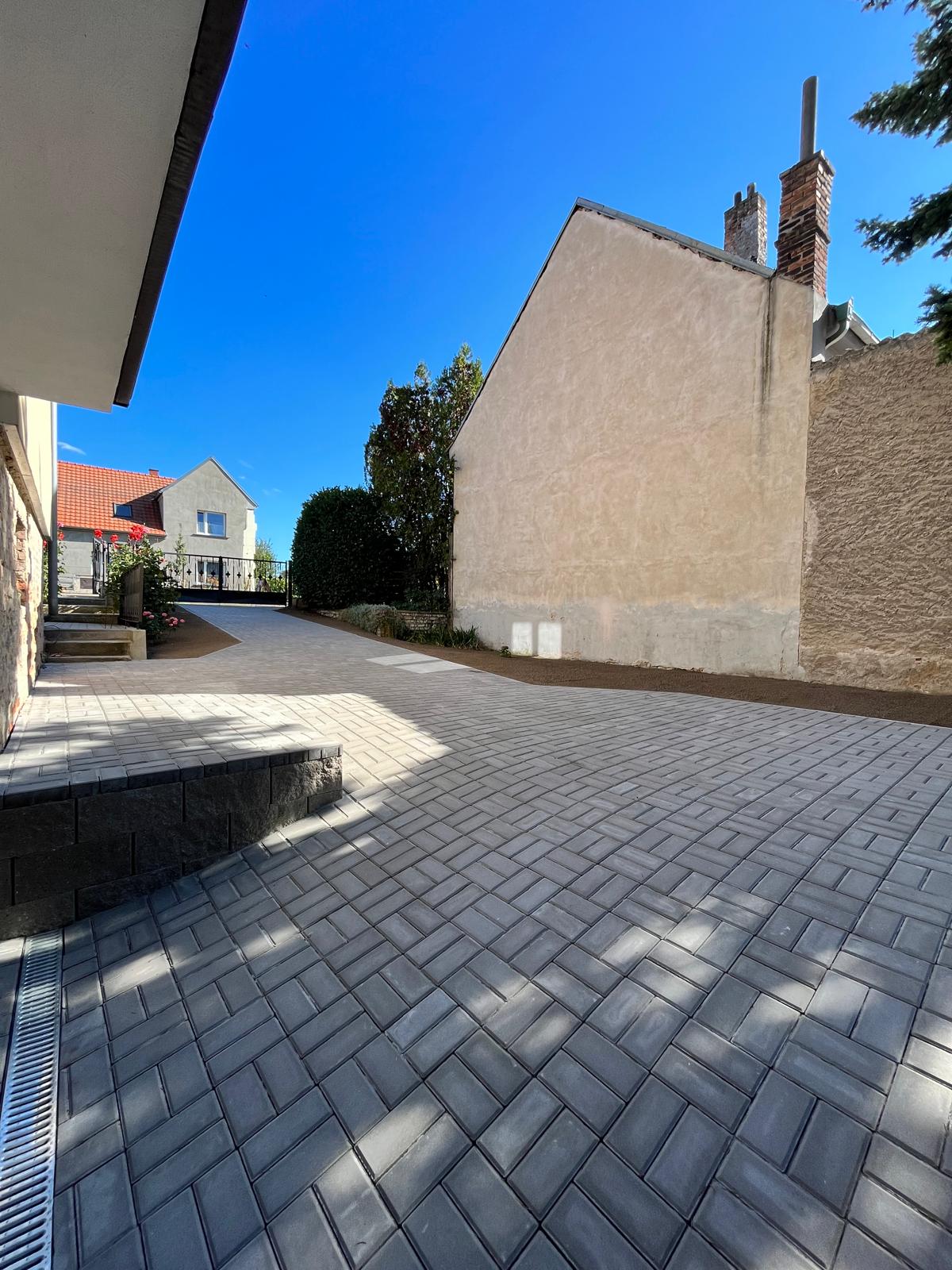 Dlážděná příjezdová cesta s budovami a modrou oblohou. Venkovní zpevněná plocha v slunečném dni. Architektura a nemovitosti.