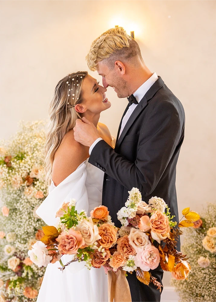 Bride and groom touching noses with a peach and white bouquet