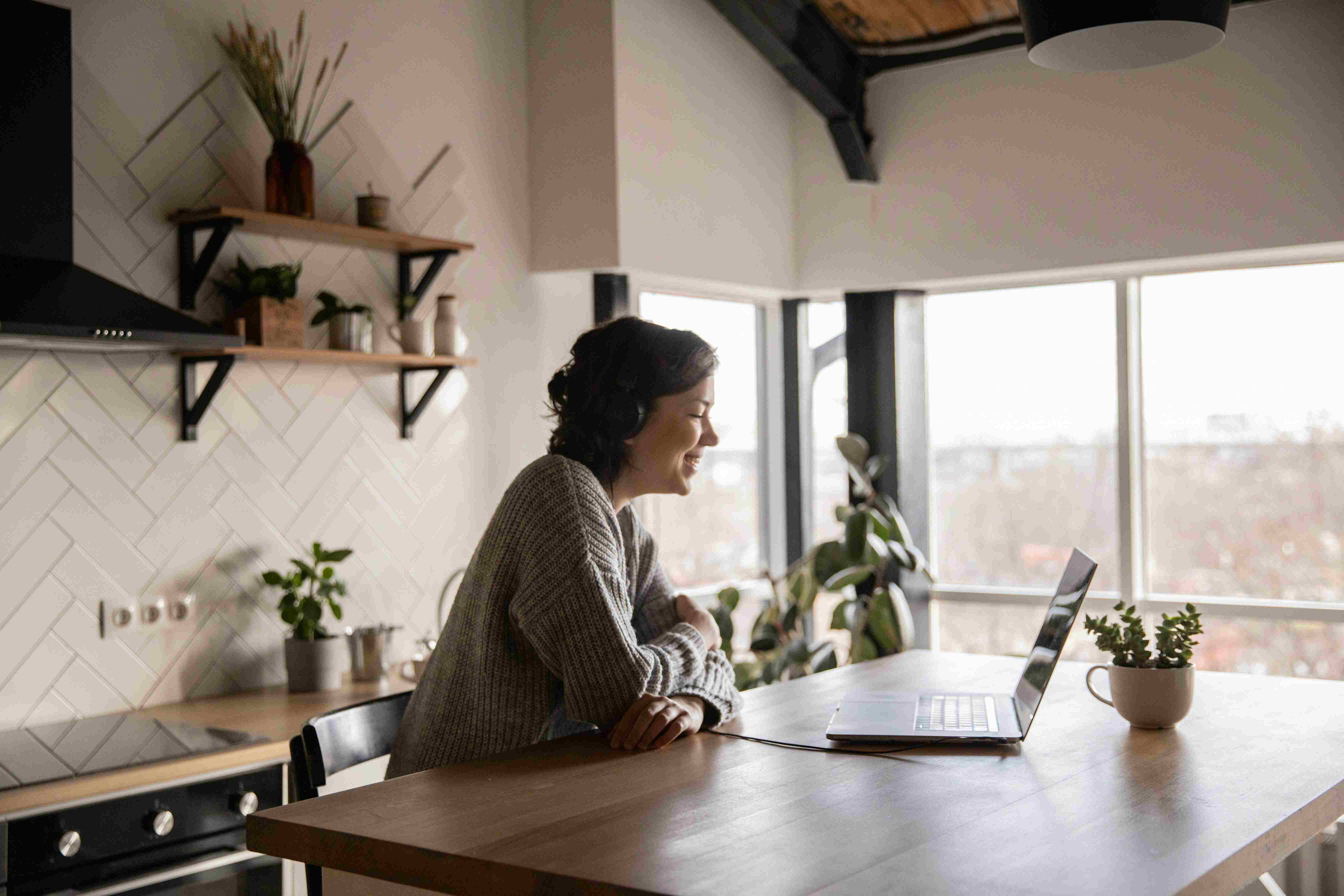 Smiling professional woman in a white blazer sitting at a desk with a laptop, offering a welcoming and expert consultation.