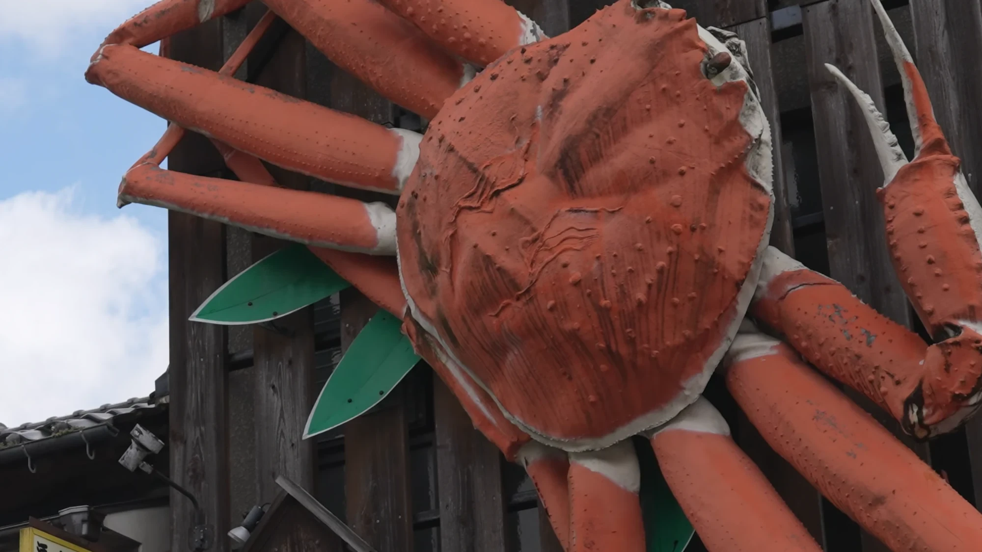 An oversized model snow crab mounted above a Kinosaki shopfront against a blue sky.