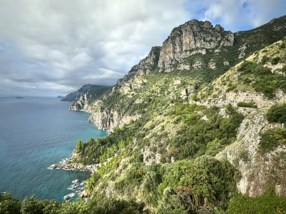 Steep green cliffs dropping into clear turquoise water along the Amalfi Coast road.