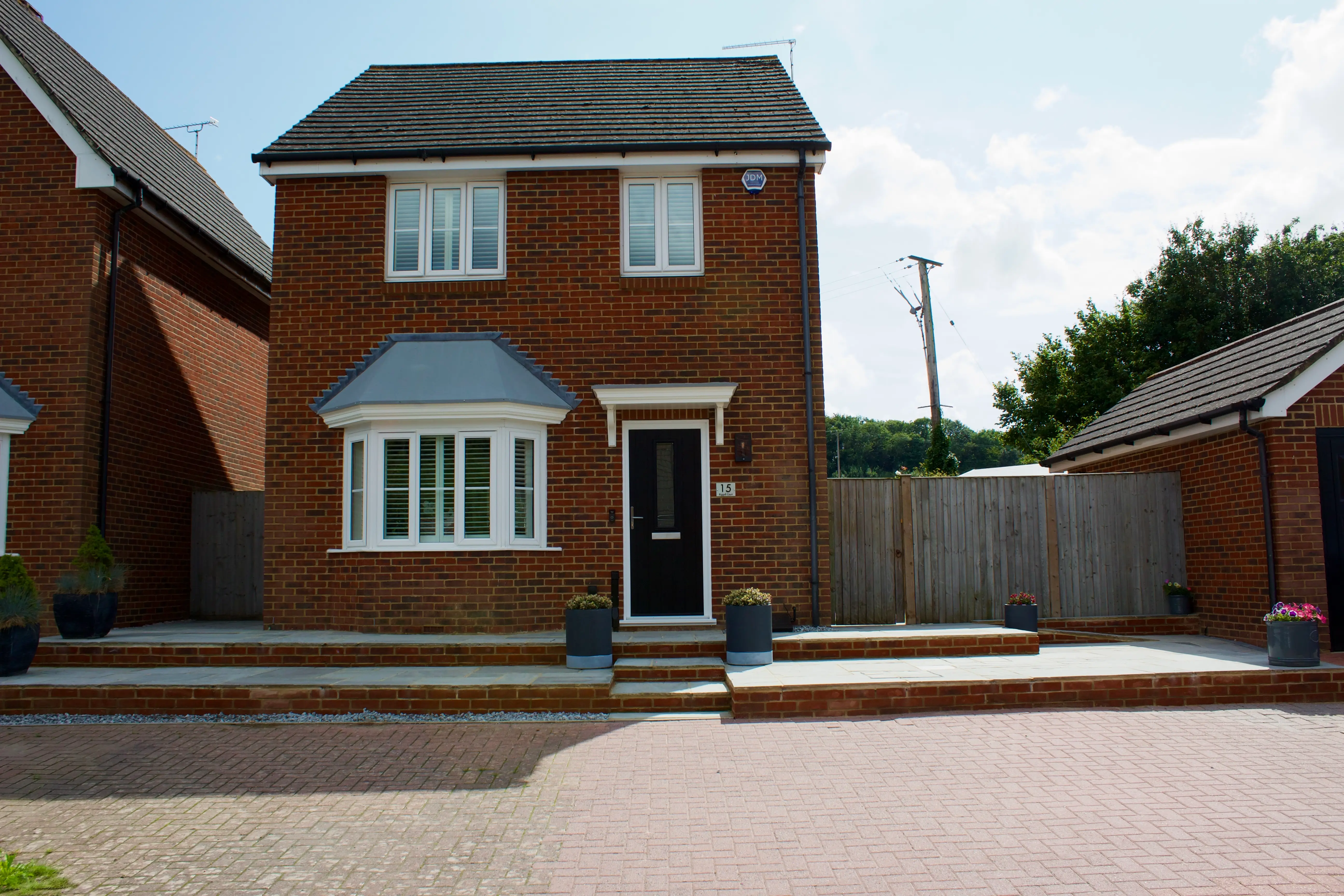 A two-story brick house with a front yard and steps leading to the entrance, surrounded by a fence.