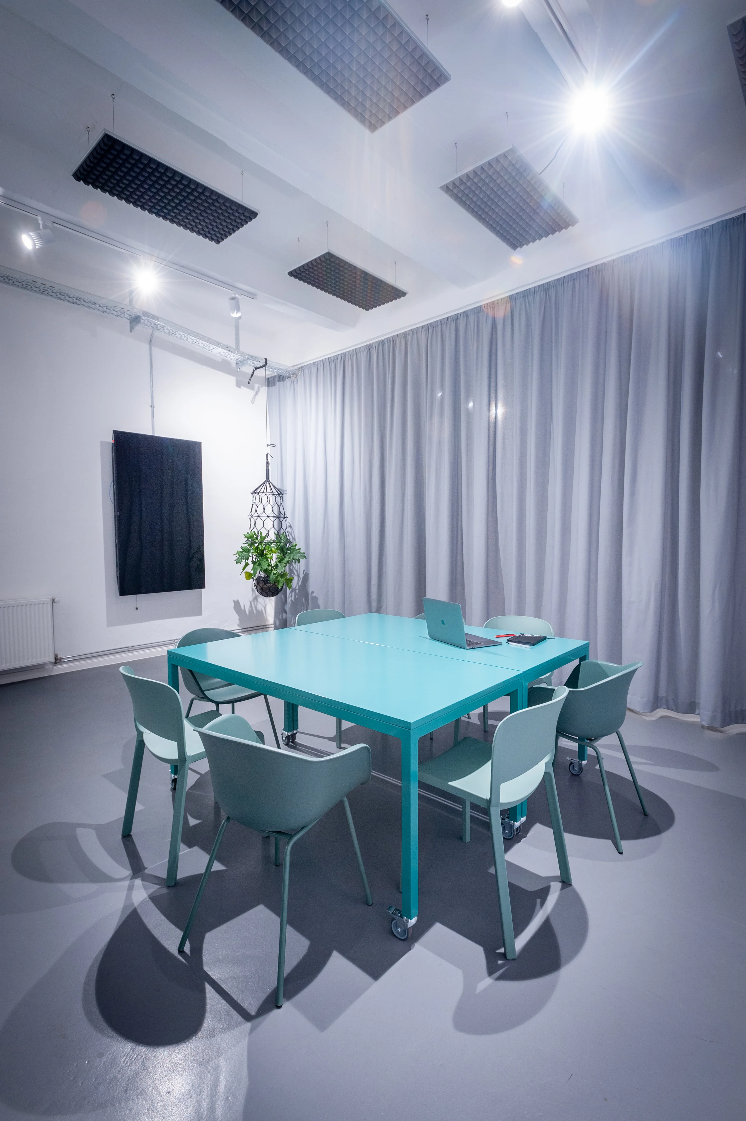 Meeting room at HEY CONTENT STUDIO with a turquoise table on castors, sage-green shell chairs, a black presentation screen and grey curtain walls.