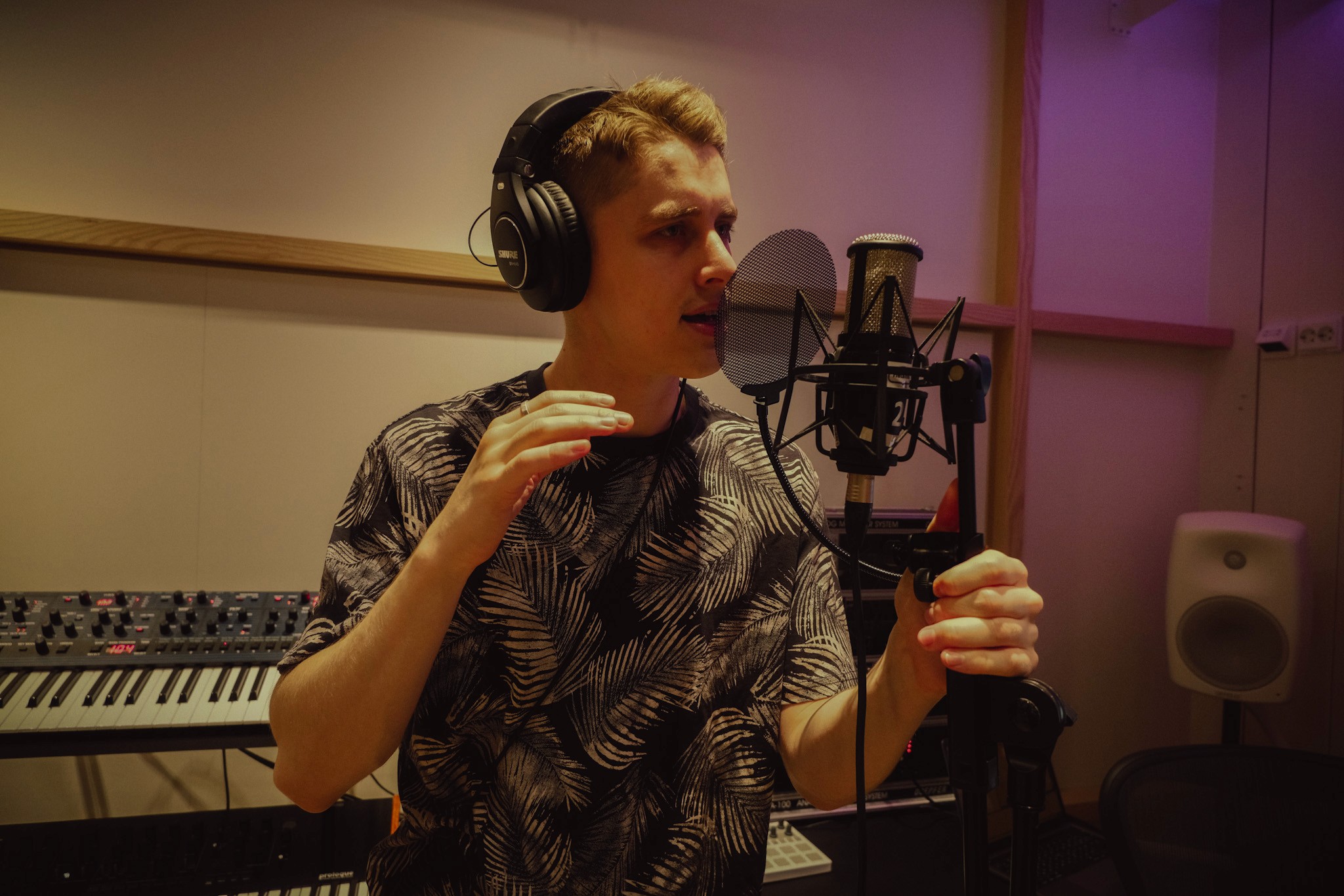 A musician recording vocals in a studio, wearing headphones and gesturing passionately.