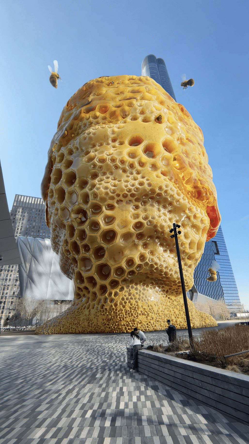 A massive, glowing honeycomb structure in the shape of a head stands in a city plaza for a Gisou activation