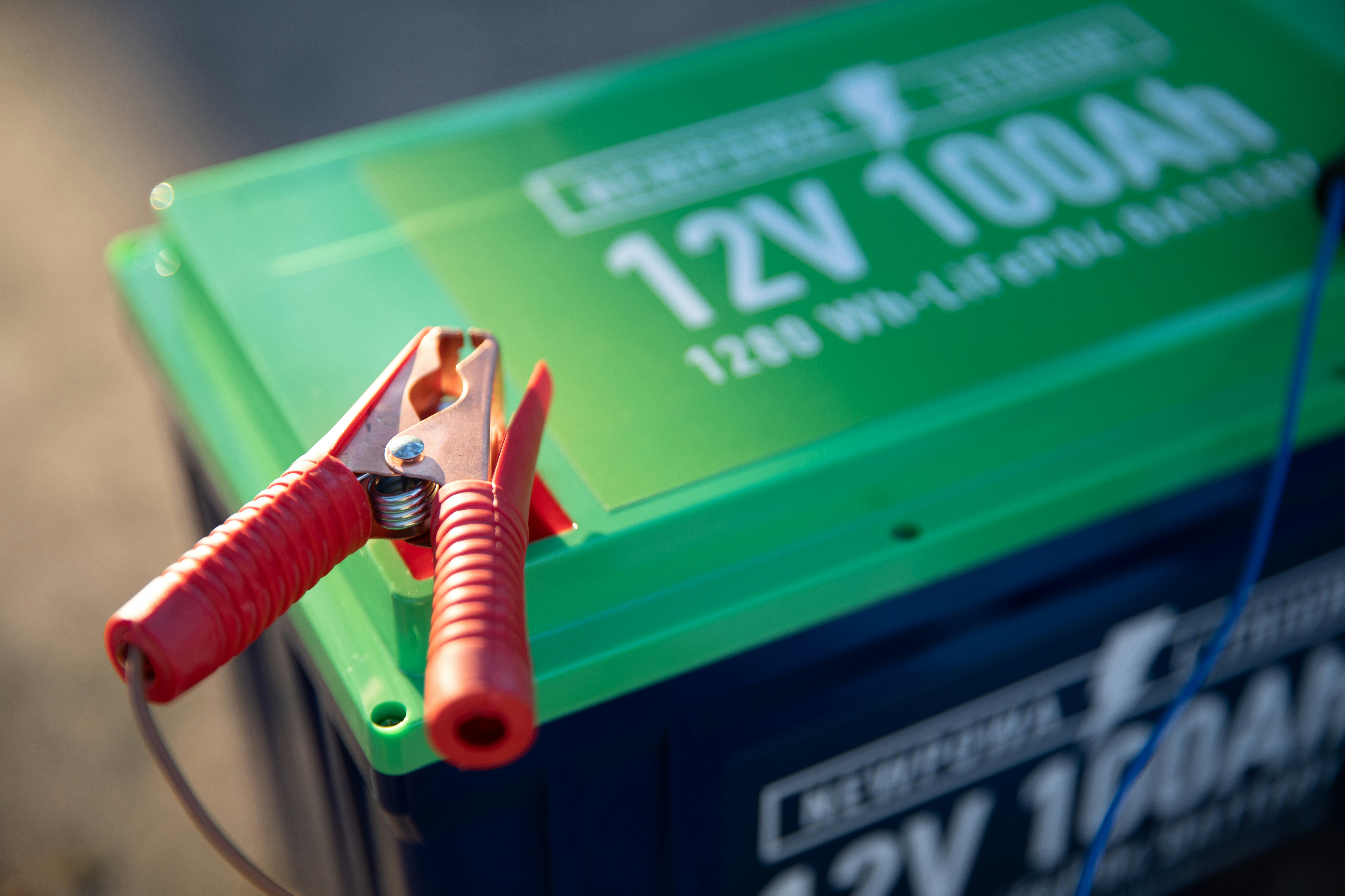 a red and green battery with a pair of pliers attached to it