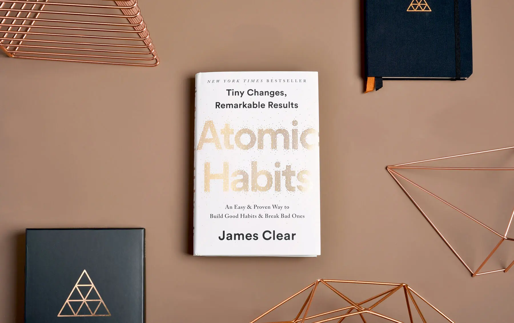 Atomic Habits by James Clear book cover on a tan background, referenced for habit-formation principles in building resilience