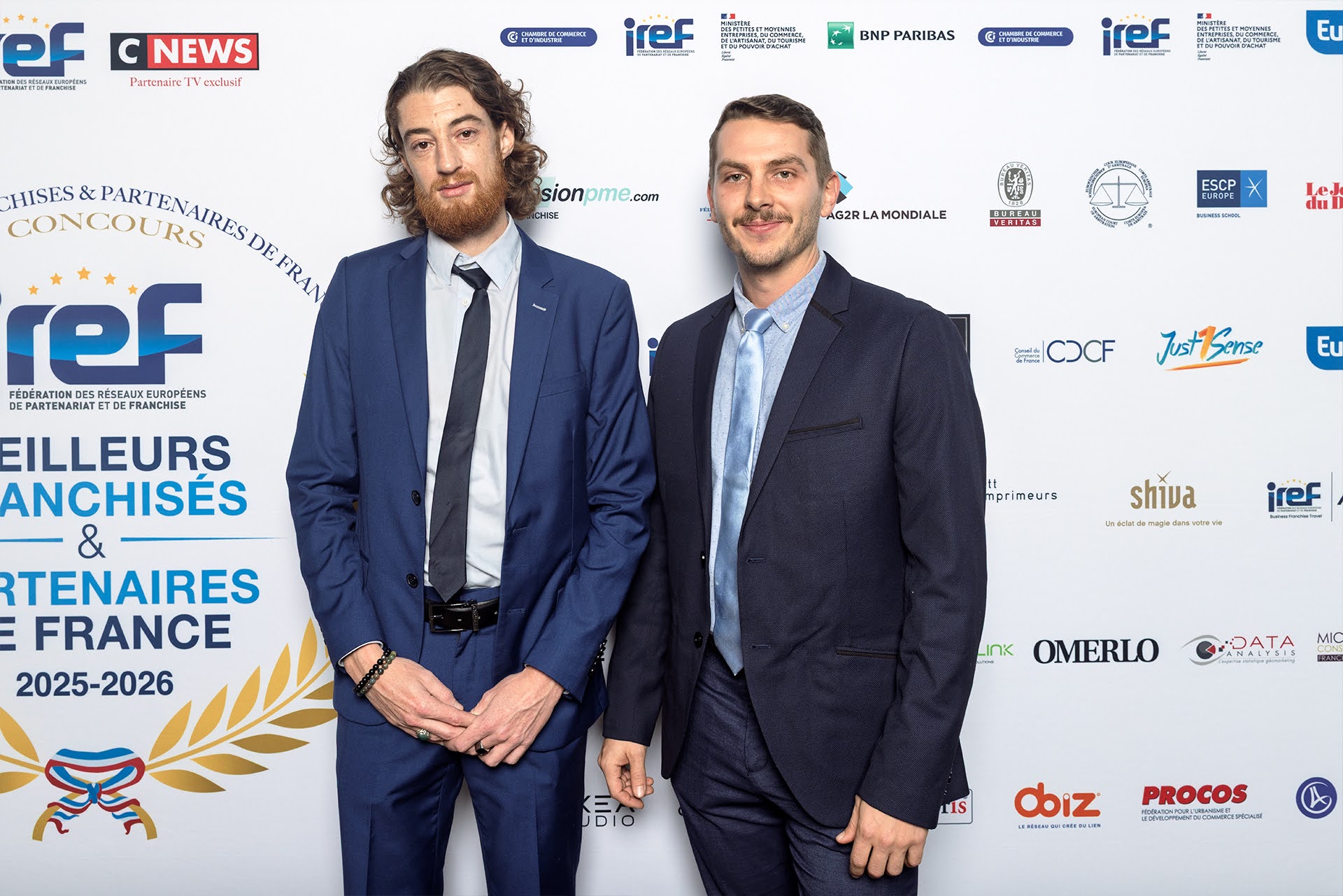 A smiling woman with her arms crossed, standing against a dark green background. She has long, dark hair.