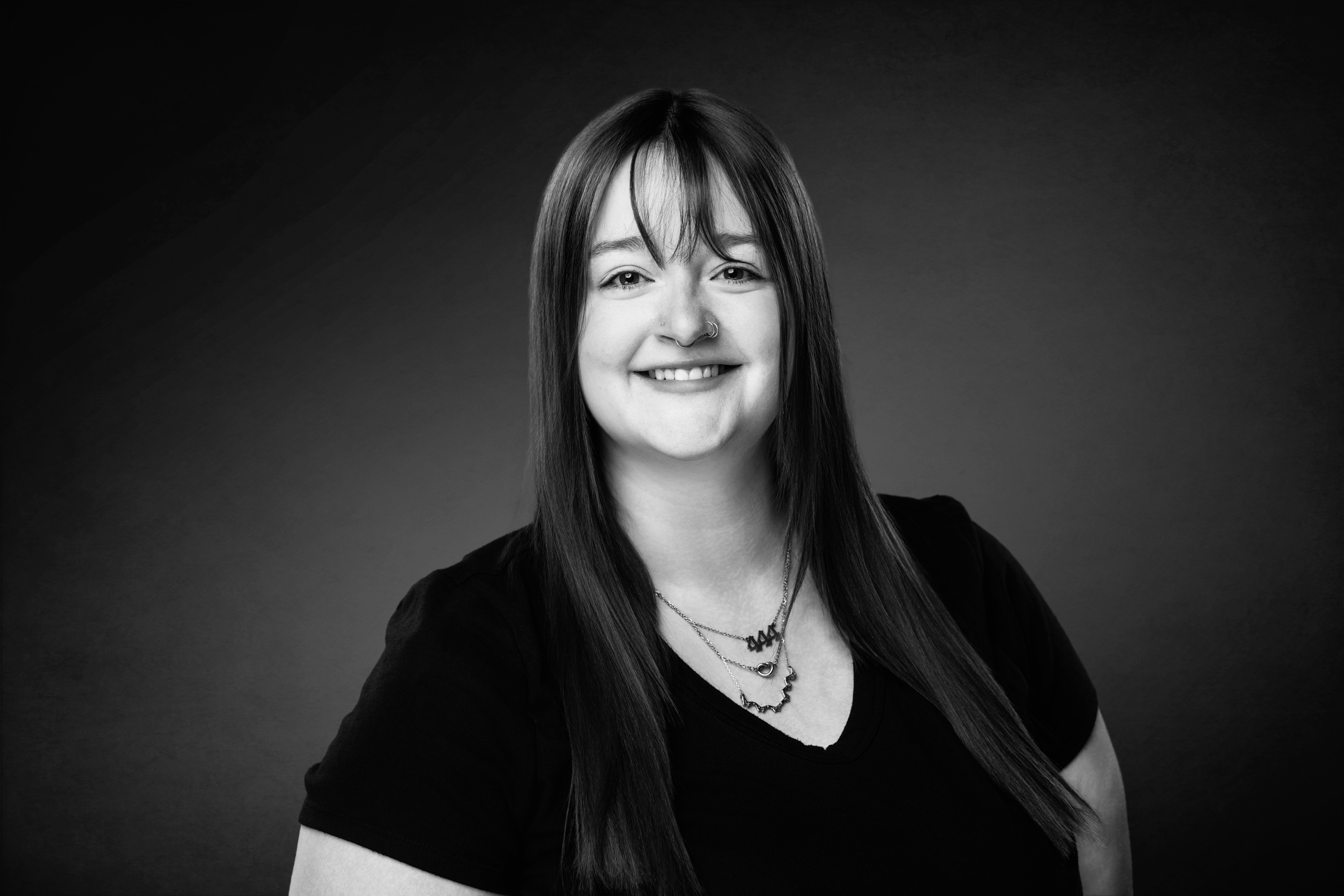 A thoughtful young person with dark hair gazes to the side, captured in soft black and white lighting.
