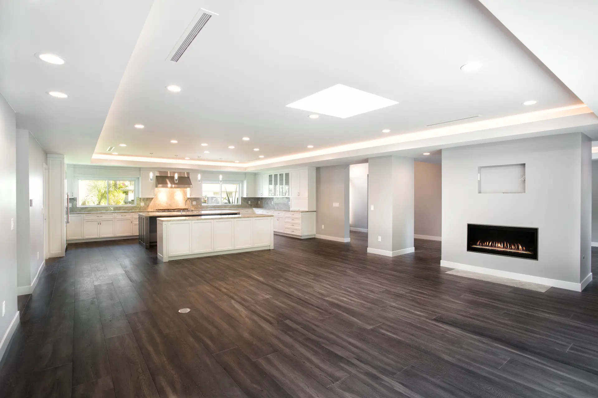 Spacious living room with rich wooden flooring, recessed lighting, and a sleek fireplace, open to kitchen in Costa Mesa Remodel. Photo by Chris Darnall.