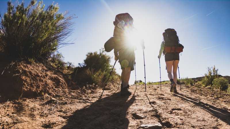 Two hikers are walking towards the sun