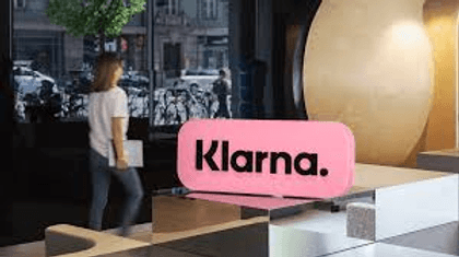 Pinkes Klarna-Schild im Eingangsbereich, eine Frau geht vorbei, Cover zu Klarnas Problemen und der BNPL-Korrektur