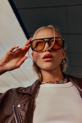Fotografia portretowa blondynki dotykającej okulary przeciwsłoneczne.