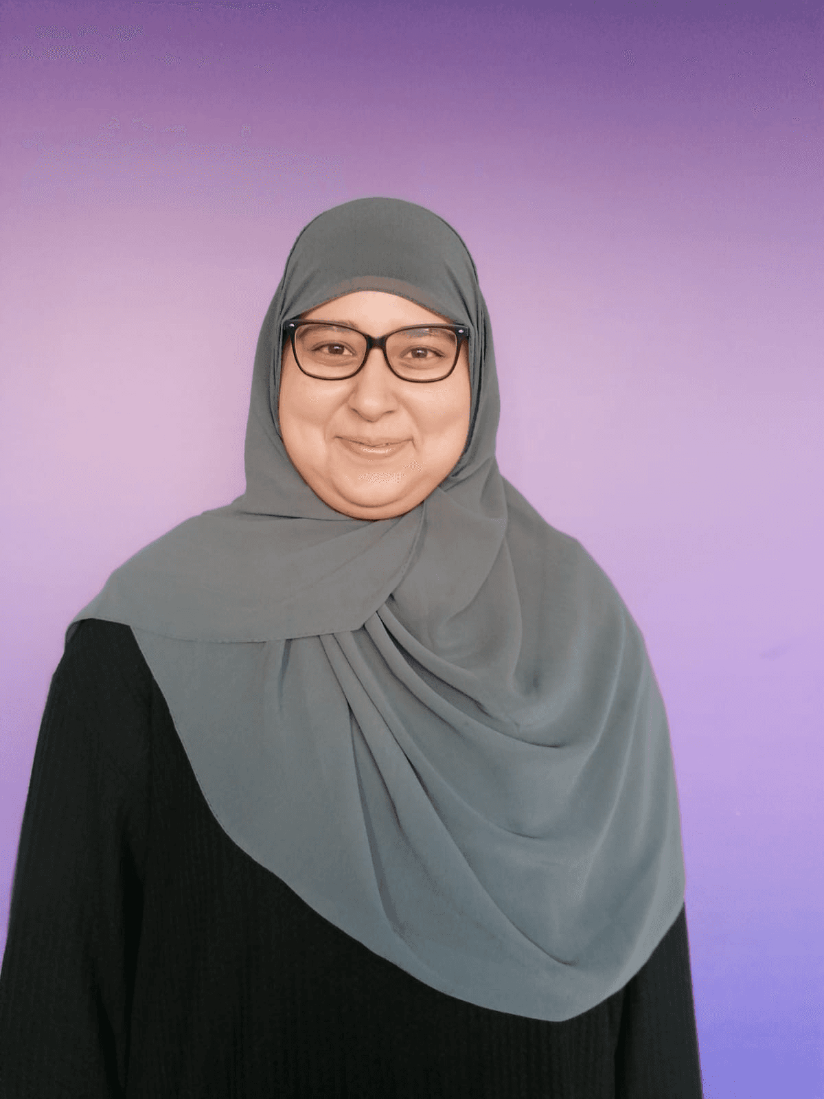 Two women on bicycles smile and chat while riding on a tree-lined path. One wears a floral dress, the other a white jacket and pants.