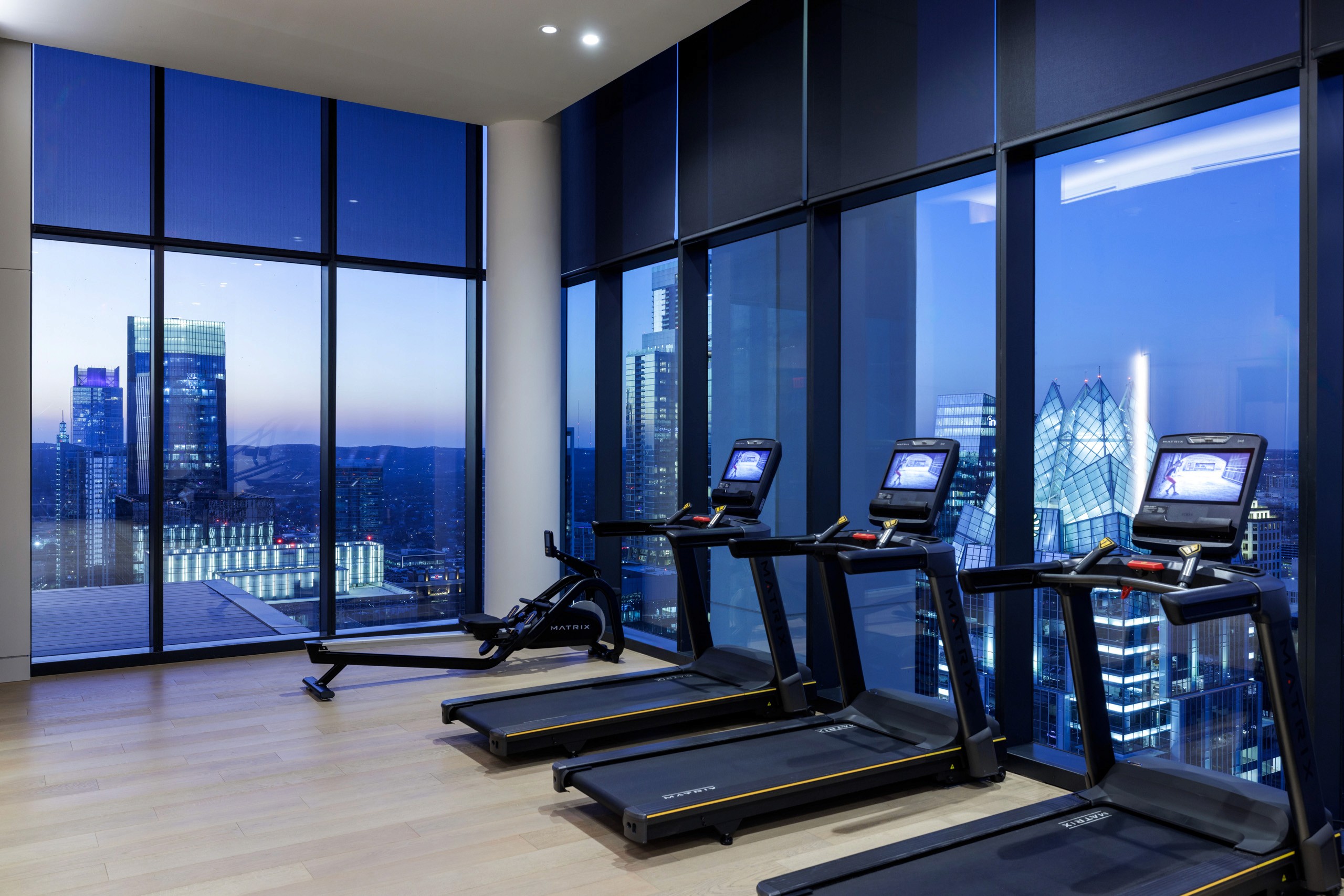 Gym with treadmills and rowing machine overlooking cityscape at dusk