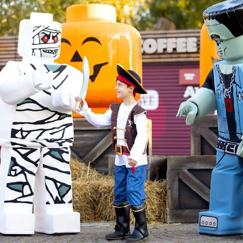 Dijete u gusarskom kostimu komunicira s LEGO figurama mumije i Frankensteina u prirodnoj veličini u ambijentu s temom Noći vještica.